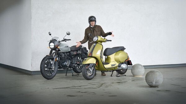 Mann mit fragender Gestik steht zwischen Motorrad und Roller