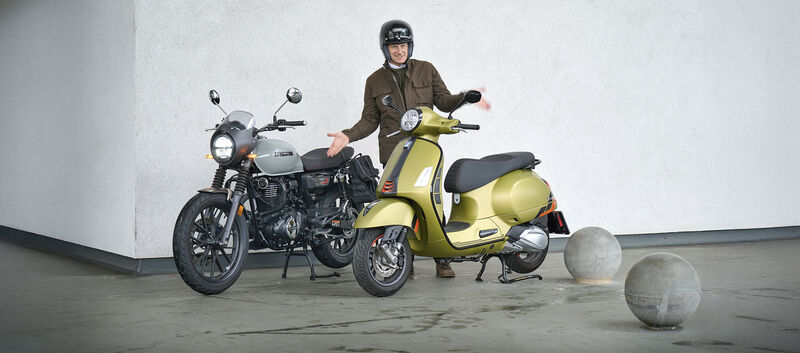 Mann mit fragender Gestik steht zwischen Motorrad und Roller