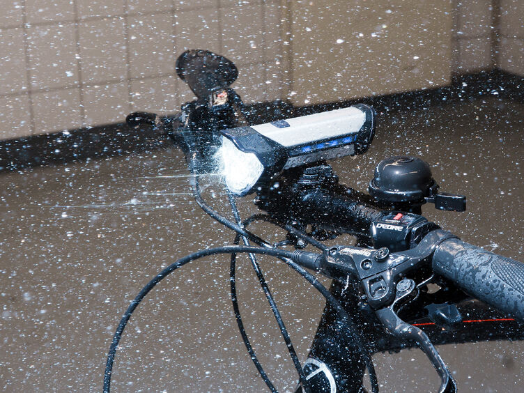 Ein Fahrrad steht in einem Labor im künstlichen Regen mit aktivierter Beleuchtung.