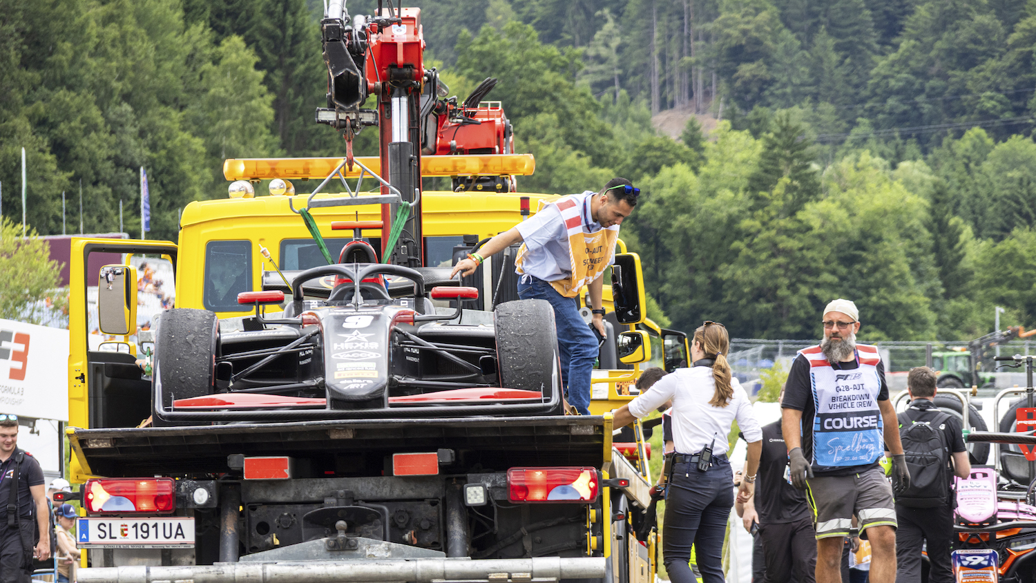 Ein Formel-Auto wird auf einem Lkw abgeschleppt, auf dem sich auch ein technischer Kommissar befindet.