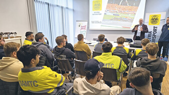 Eine Person im Sakko hält vor vielen Personen einen Vortrag.