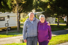 Das Bild ist ein Foto von Familie Gernhardt, bestehend aus zwei Personen, ein Mann und einer Frau. Sie stehen arm in Arm, im Hintergrund ist ein Campingfahrzeug zu sehen.