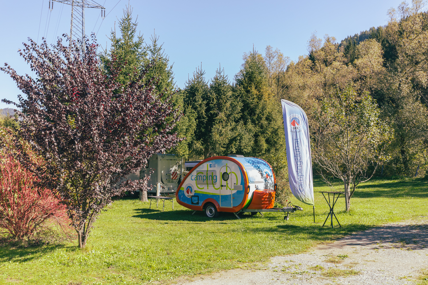 Auf dem Foto sieht man den ÖCC Camping-Anhänger der auf einer Wiese steht umringt von Bäumen und Sträuchern.