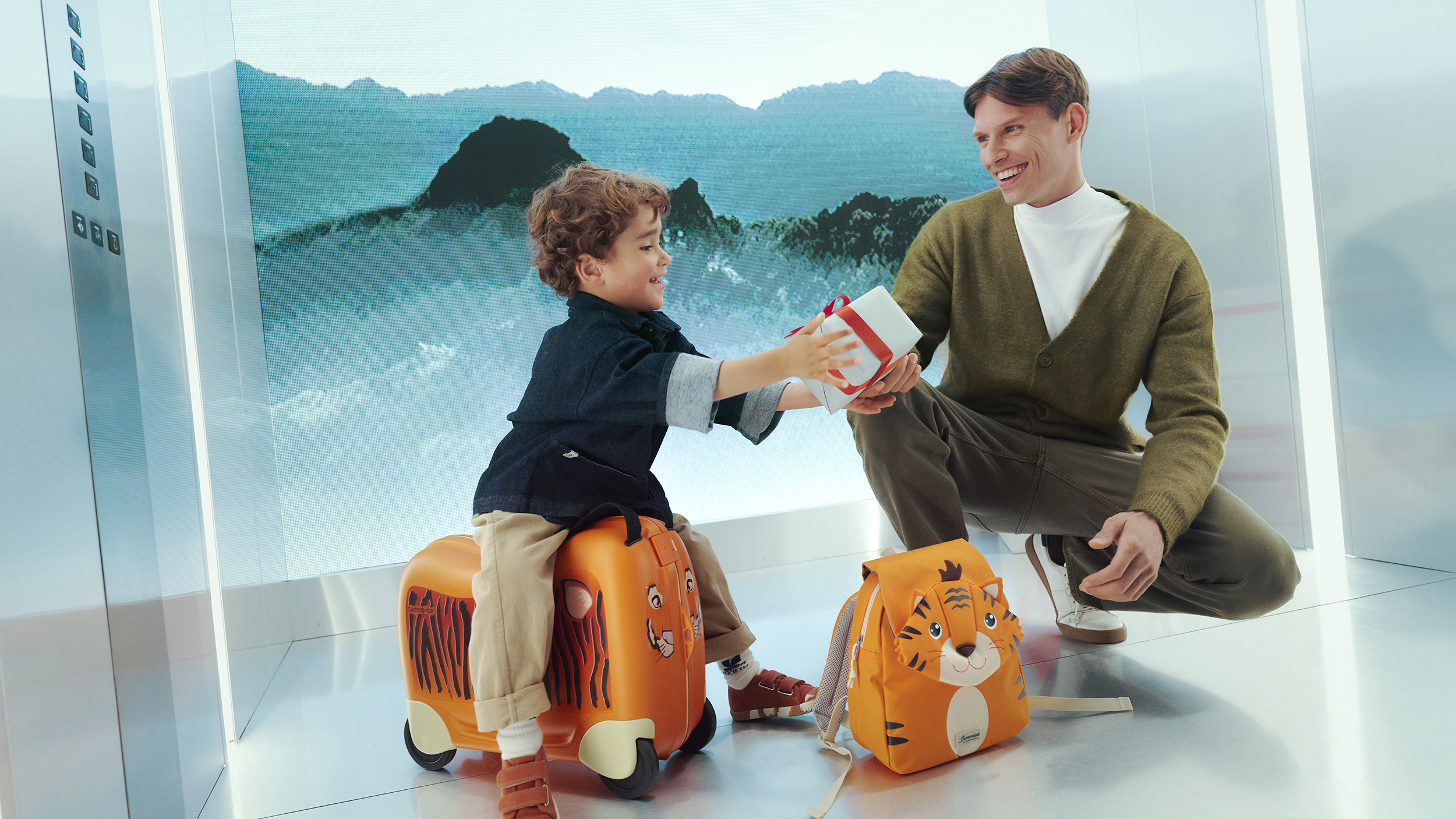 Imagebild Samsonite: Ein Kind sitzt auf einem kleinen Koffer mit Rollen im Tiger-Design daneben steht ein kleiner Tiger-Rucksack und ein Erwachsener hockerlt daneben.