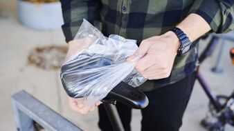 Hände, die über einen Fahrradsitz ein Plastiksackerl ziehen.