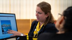 Auf dem Bild sieht man eine Dame vor einem Computerbildschirm, die einer anderen etwas erklärt.