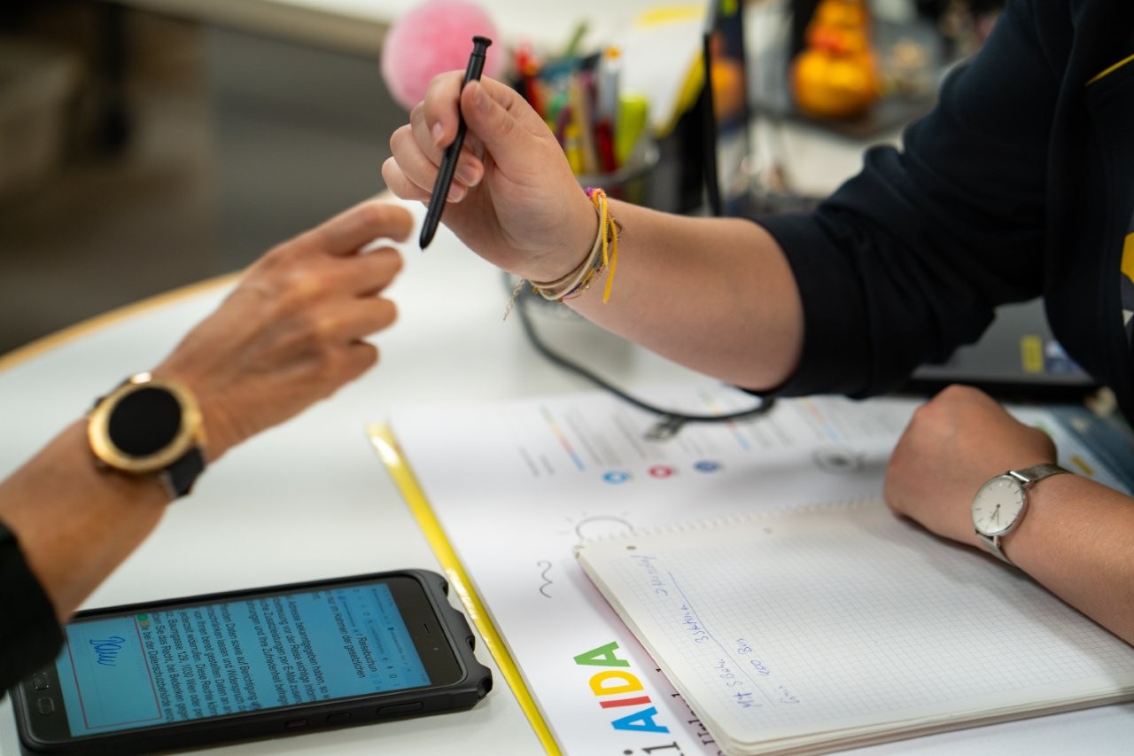 Auf dem Bild sieht man zwei Hände. Die eine gibt einen Kugelschreiber an die andere weiter.