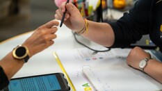 Auf dem Bild sieht man zwei Hände. Die eine gibt einen Kugelschreiber an die andere weiter.