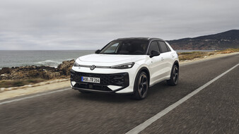 Ein weißer VW T-Roc fährt über eine Küstenstraße.