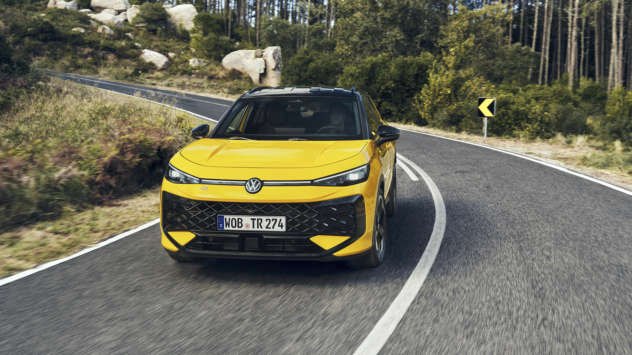 Ein gelber VW T-Roc fährt über eine Landstraße im Wald.