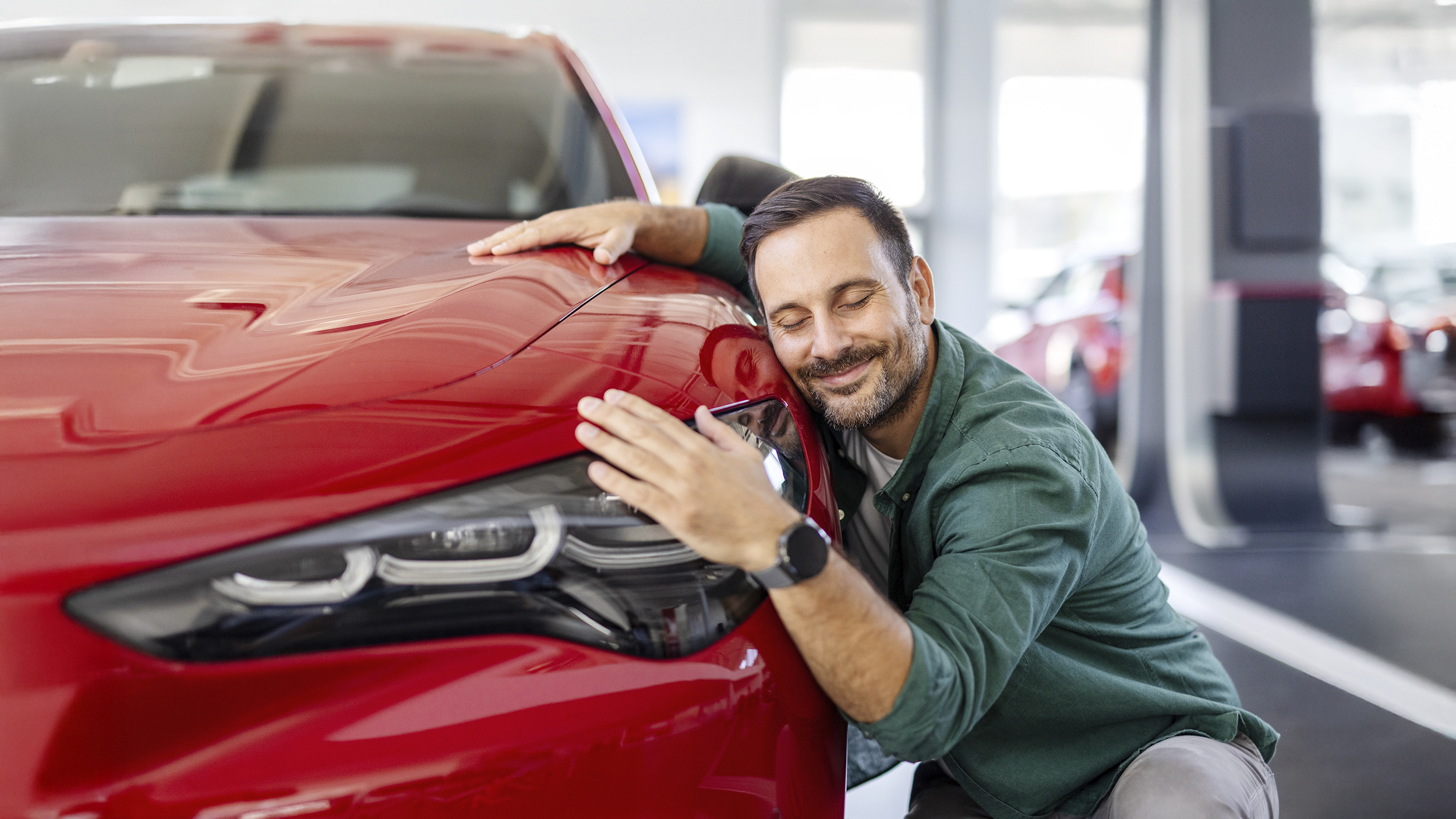Ein Mann kuschelt lächelnd mit einem roten Auto