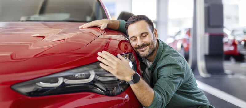Ein Mann kuschelt lächelnd mit einem roten Auto