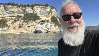 Ein Mann mit Bart steht vor den Klippen am Meer.