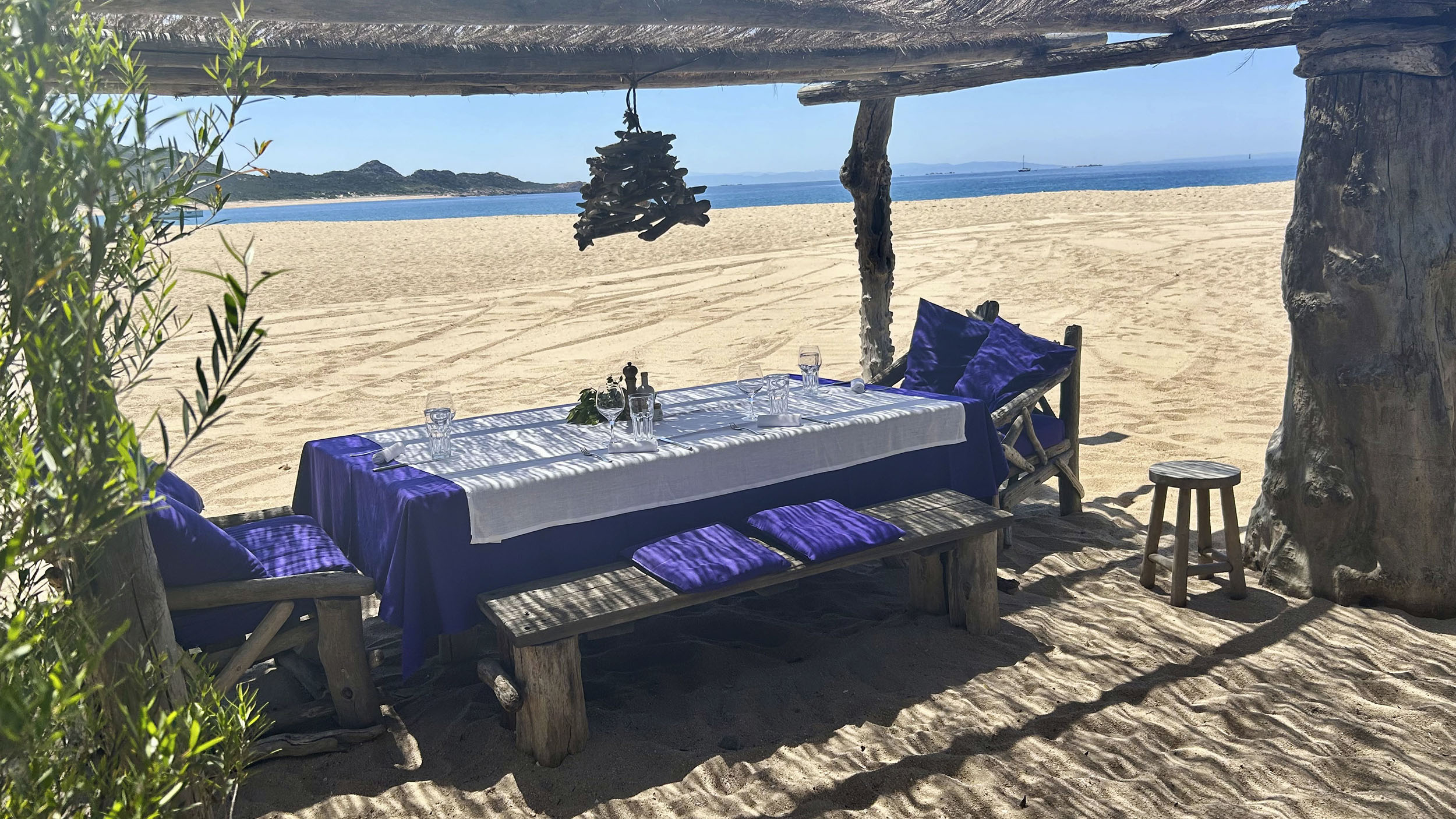Gedeckter Holztisch am Strand mit Blick aufs Meer.