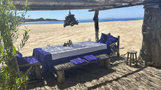 Gedeckter Holztisch am Strand mit Blick aufs Meer.