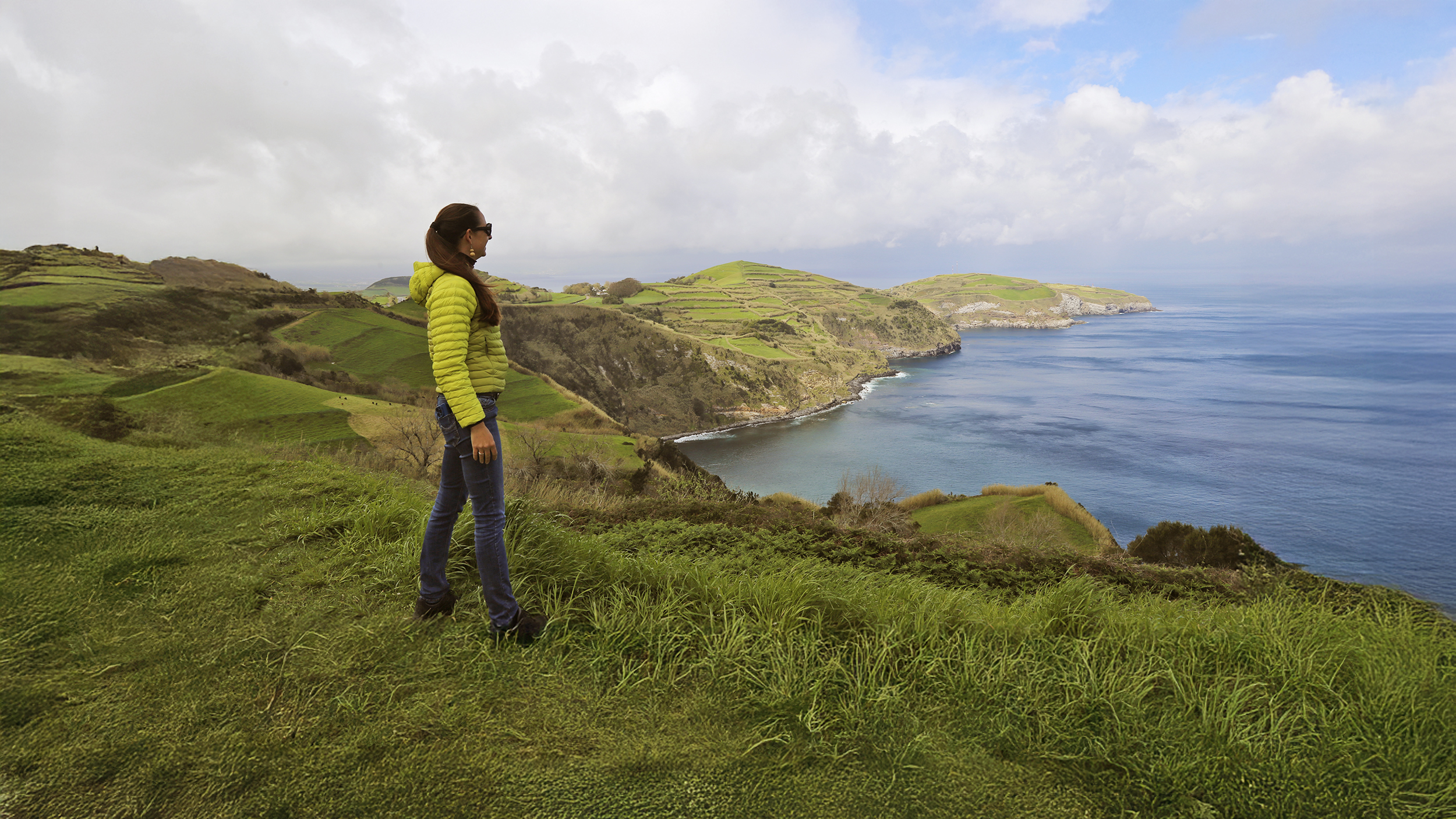  Eine Dame steht an der grünen Küste von Sao Miguel und schaut aufs Meer.