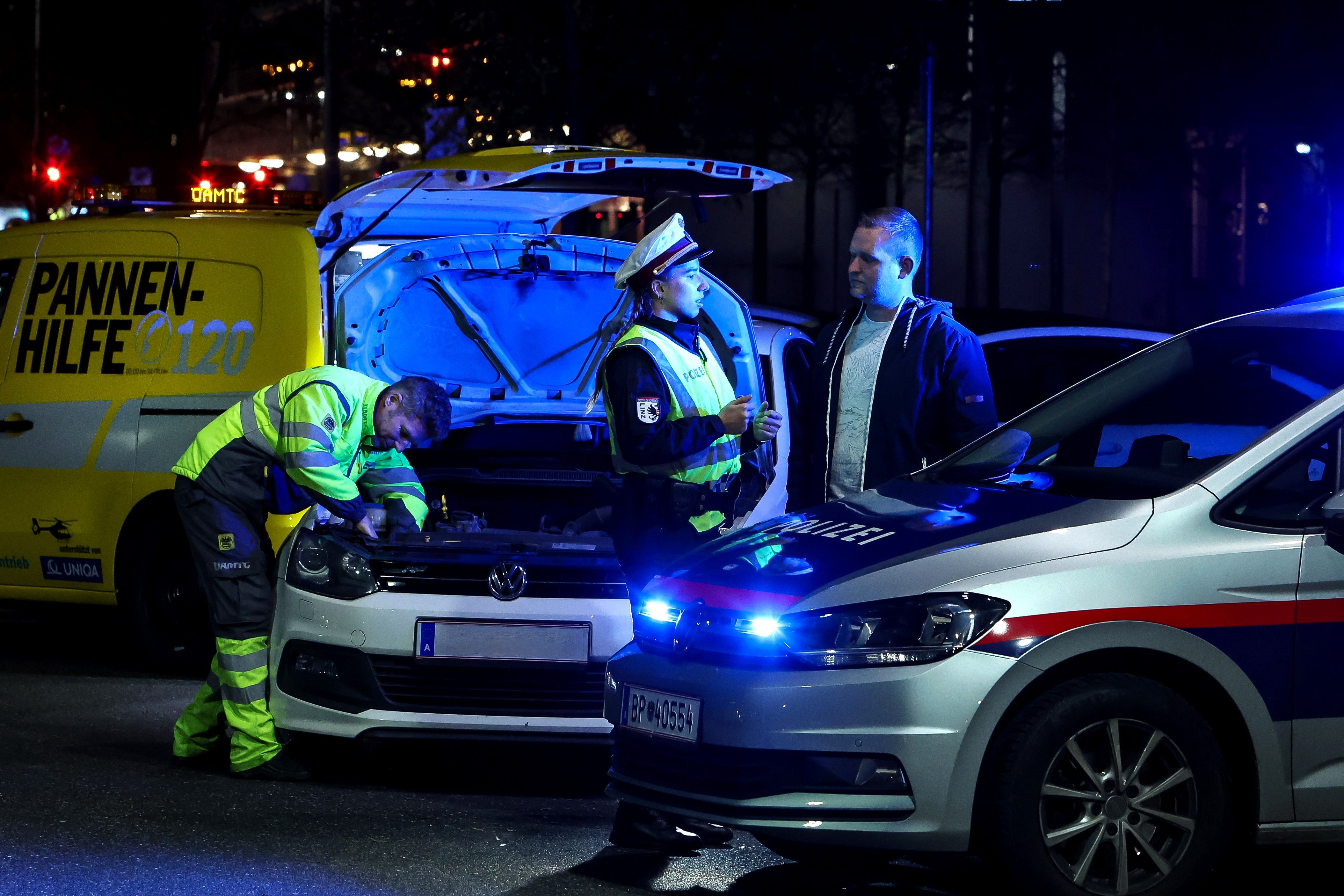 Polizistin klärt Autofahrenden über die Wichtigkeit einer ausreichenden Beleuchtung auf. Im Hintergrund wird von einem ÖAMTC-Techniker die Lampe beim Auto getauscht. Die gemeinsame Aktion nennt sich Licht statt Strafe.
