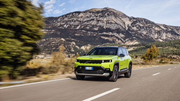 Ein grüner Jeep Compass fährt über eine Landstraße mit Hügeln im Hintergrund.