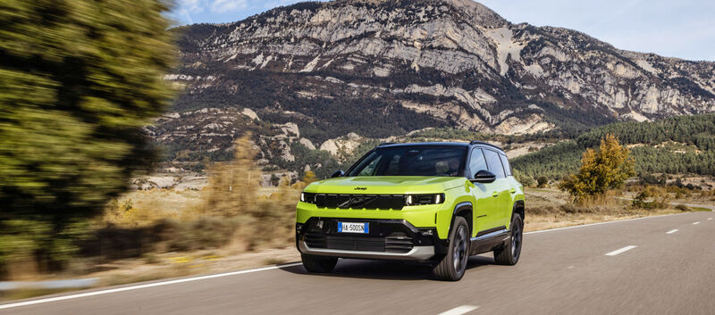 Ein grüner Jeep Compass fährt über eine Landstraße mit Hügeln im Hintergrund.
