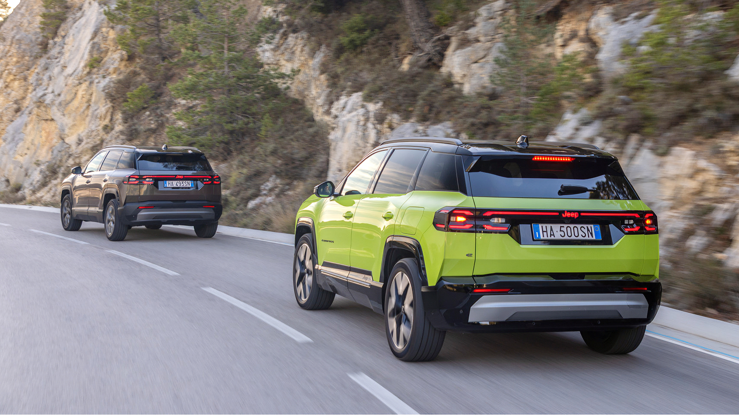 Ein grauer und ein grüner Jeep Compass fahren auf einer Landstraße an einer Felswand vorbei.