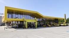 Gelbes, modern gestaltetes ÖAMTC-Servicegebäude in Melk mit großer Glasfront, mehreren gelben Einsatzfahrzeugen davor und Personen, die sich im Eingangsbereich unter einem Willkommensbogen versammeln.