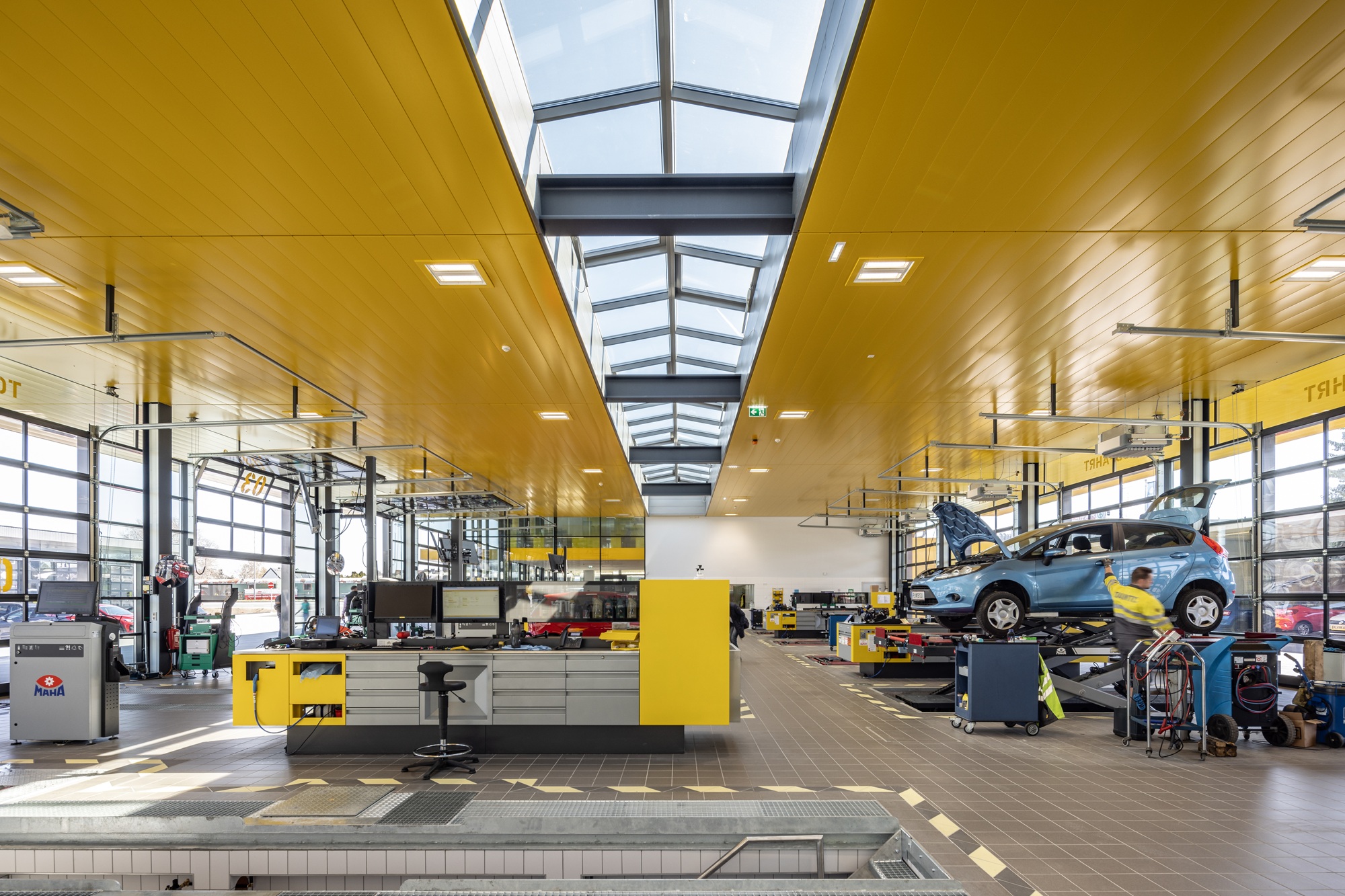 Das Bild zeigt die Prüfhalle in St. Pölten von innen. auf der linken Seite ist eine Werkbank, rechts wird gerade ein blaues Auto von einem Mitarbeiter kontrolliert. 