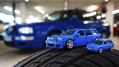 Audi-Modell aus dem Mattel Brick Shop von oben. Daneben steht das gleiche Modell von Hot Wheels. Beide stehen auf einem echten Reifen, im Hintergrund der original Audi..