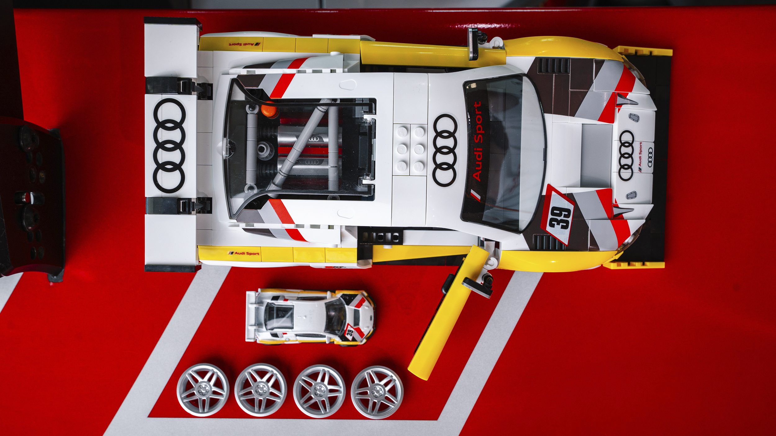 Audi R8 Sportwagen-Modell aus dem Mattel Brick Shop von oben. Daneben steht das gleiche Modell von Hot Wheels und 4 Reifen.