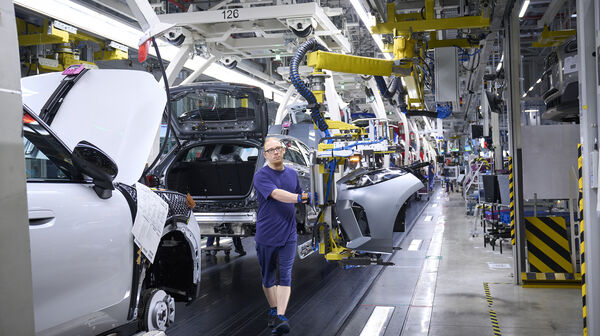 Ein blau gekleideter Mann arbeitet am Fließband in einer Autofabrik