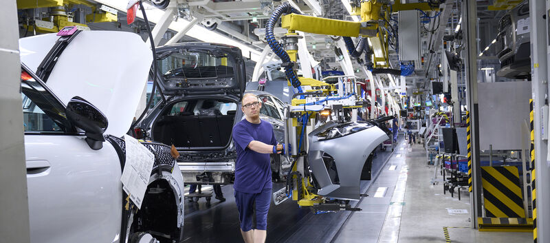 Ein blau gekleideter Mann arbeitet am Fließband in einer Autofabrik