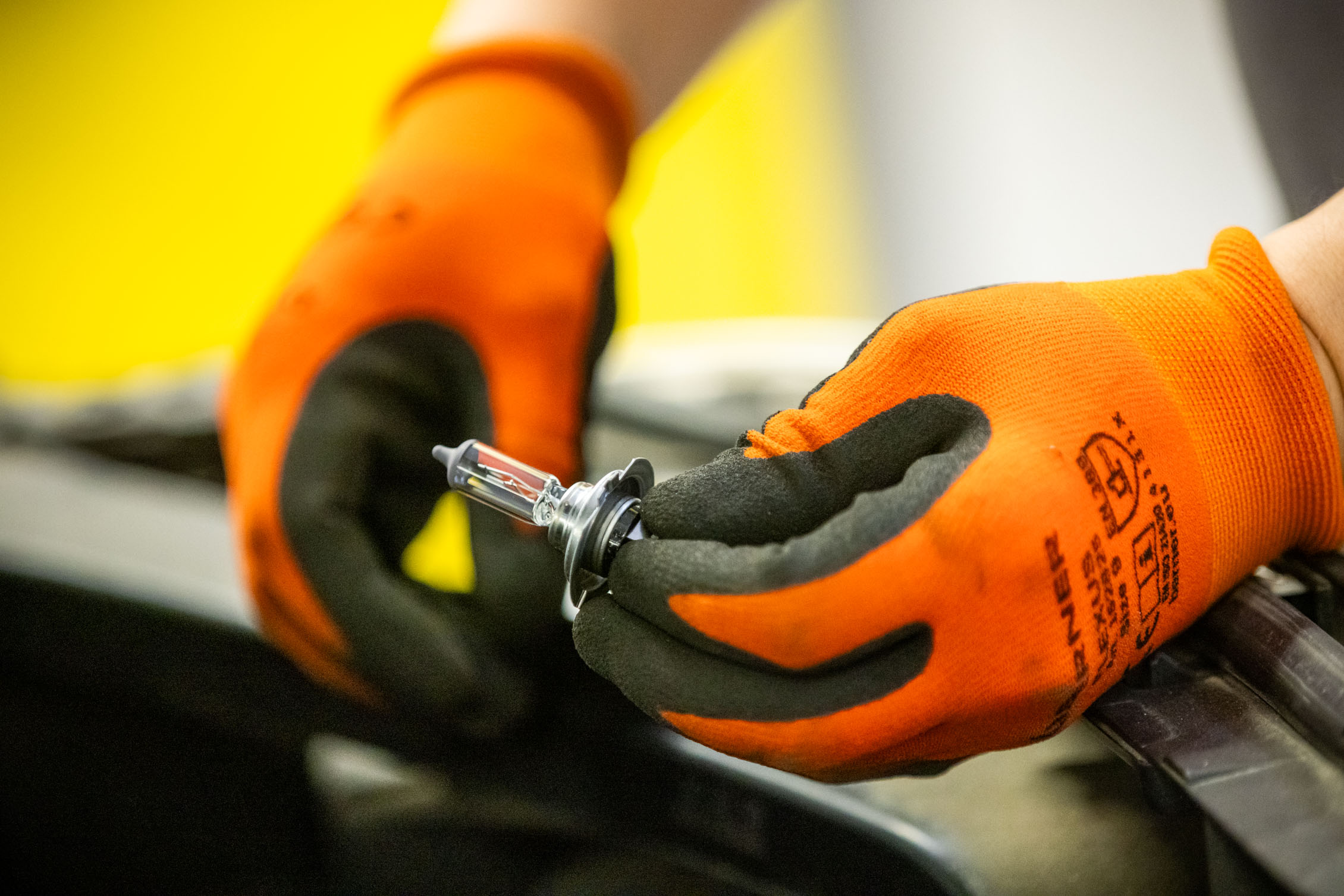 Auf dem Bild sieht man zwei Hände in orangenen Arbeitshandschuhen, die eine Fahrzeug-Lampe halten.