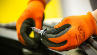 Auf dem Bild sieht man zwei Hände in orangenen Arbeitshandschuhen, die eine Fahrzeug-Lampe halten.