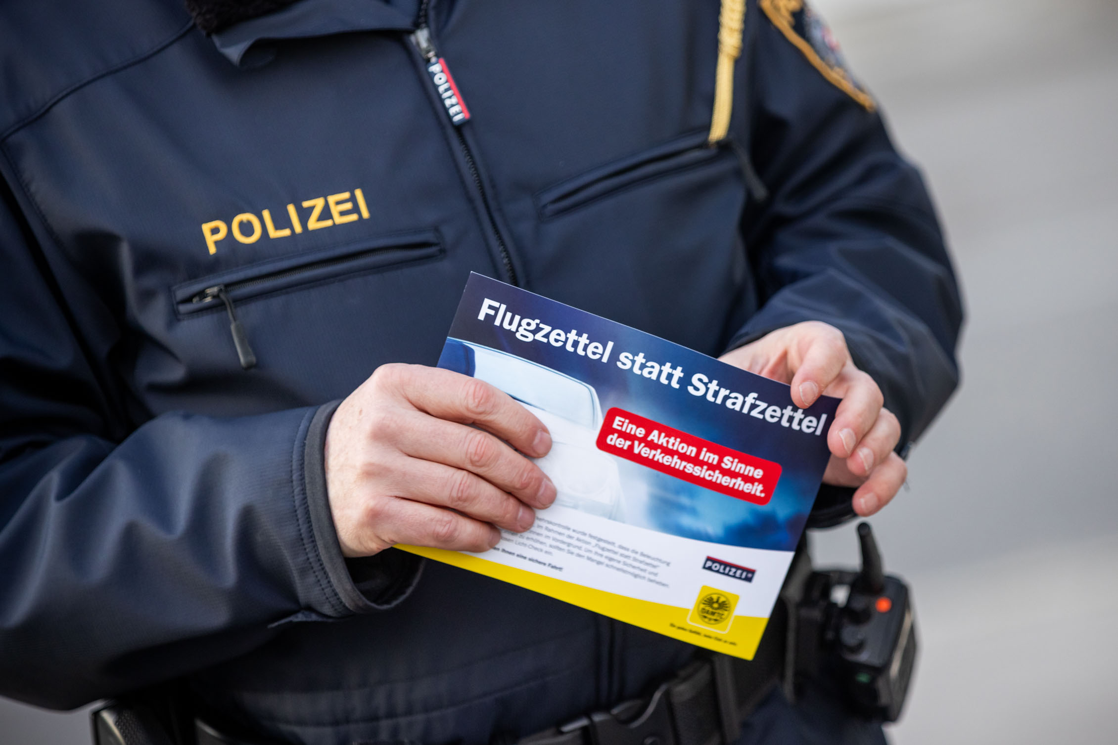 Auf dem Bild sieht man die Hände eines Polizisten, der einen Flugzettel hält, auf dem Flugzettel statt Strafzettel steht.