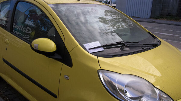 In der Winschutzscheibe eines Autos steckt ein Strafzettel hinter dem Scheibenwischer