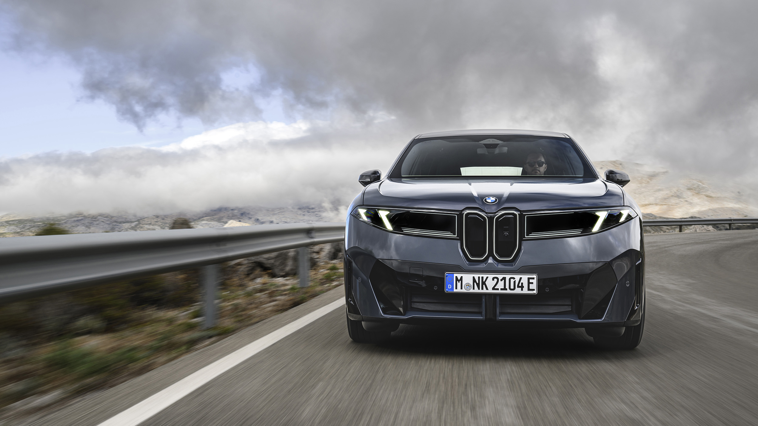 Ein dunkelgrauer BMW iX3 fährt auf einer Landstraße.