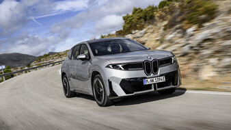 Ein BMW iX3 fährt durch eine Kurve auf einer Landstraße.