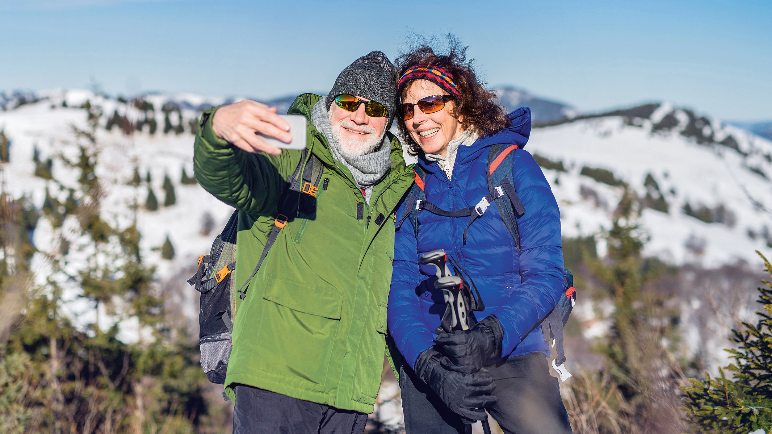 Senior couple hikers standing in snow-covered winter nature, taking selfie.