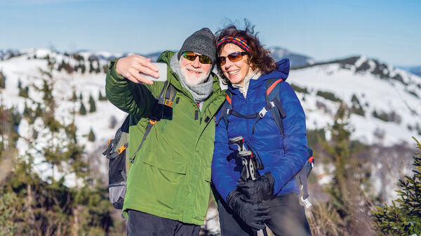 Senior couple hikers standing in snow-covered winter nature, taking selfie.
