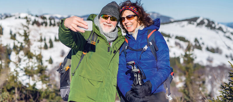 Senior couple hikers standing in snow-covered winter nature, taking selfie.
