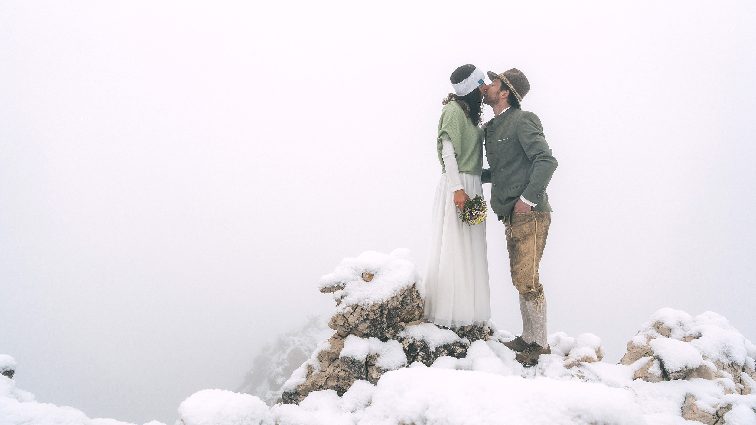 Zwei Menschen im Hochzeitsgewand küssen sich am Berg im Schnee.