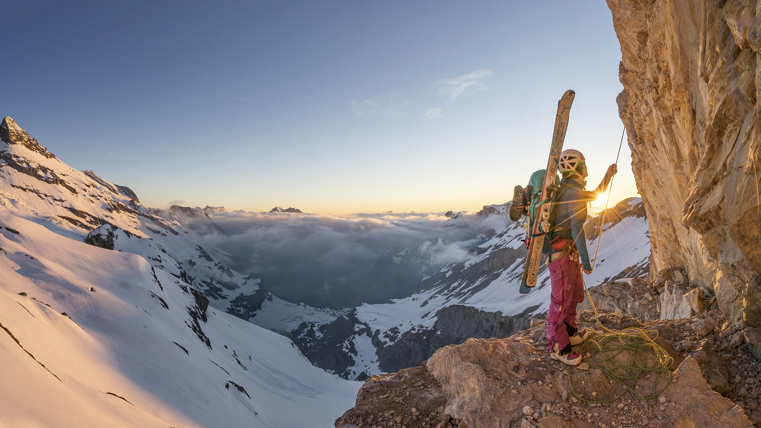 Bergsteigerin Marlies Czerny  beim Abseilen mit Skiern am Rucksack. Bergpanorama im Hintergrund.
