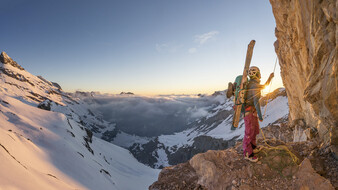 Bergsteigerin Marlies Czerny beim Abseilen mit Skiern am Rucksack. Bergpanorama im Hintergrund.