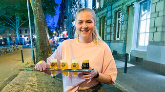 Freundliche Kellnerin serviert auf einem Brett vier Biersorten in kleinen Gläsern.