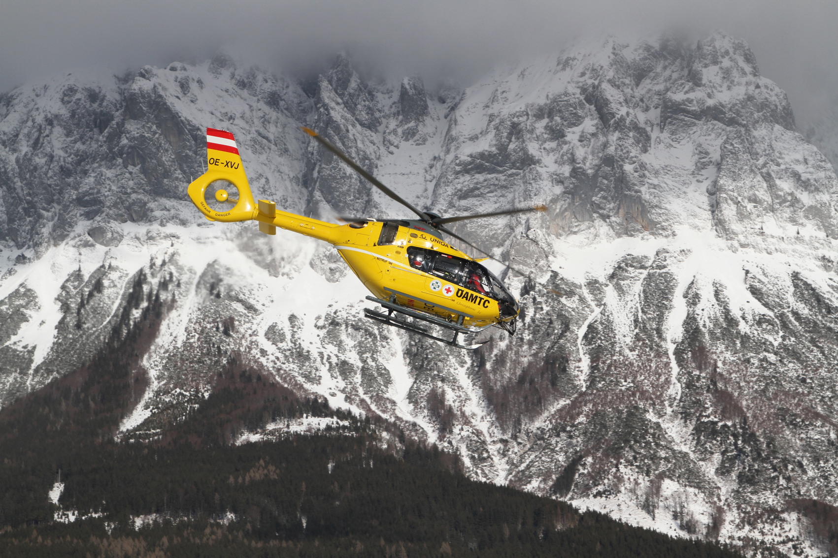 Das Bild zeigt den Hubschrauber C14, wie er vor einer schneebedeckten Bergwand fliegt.