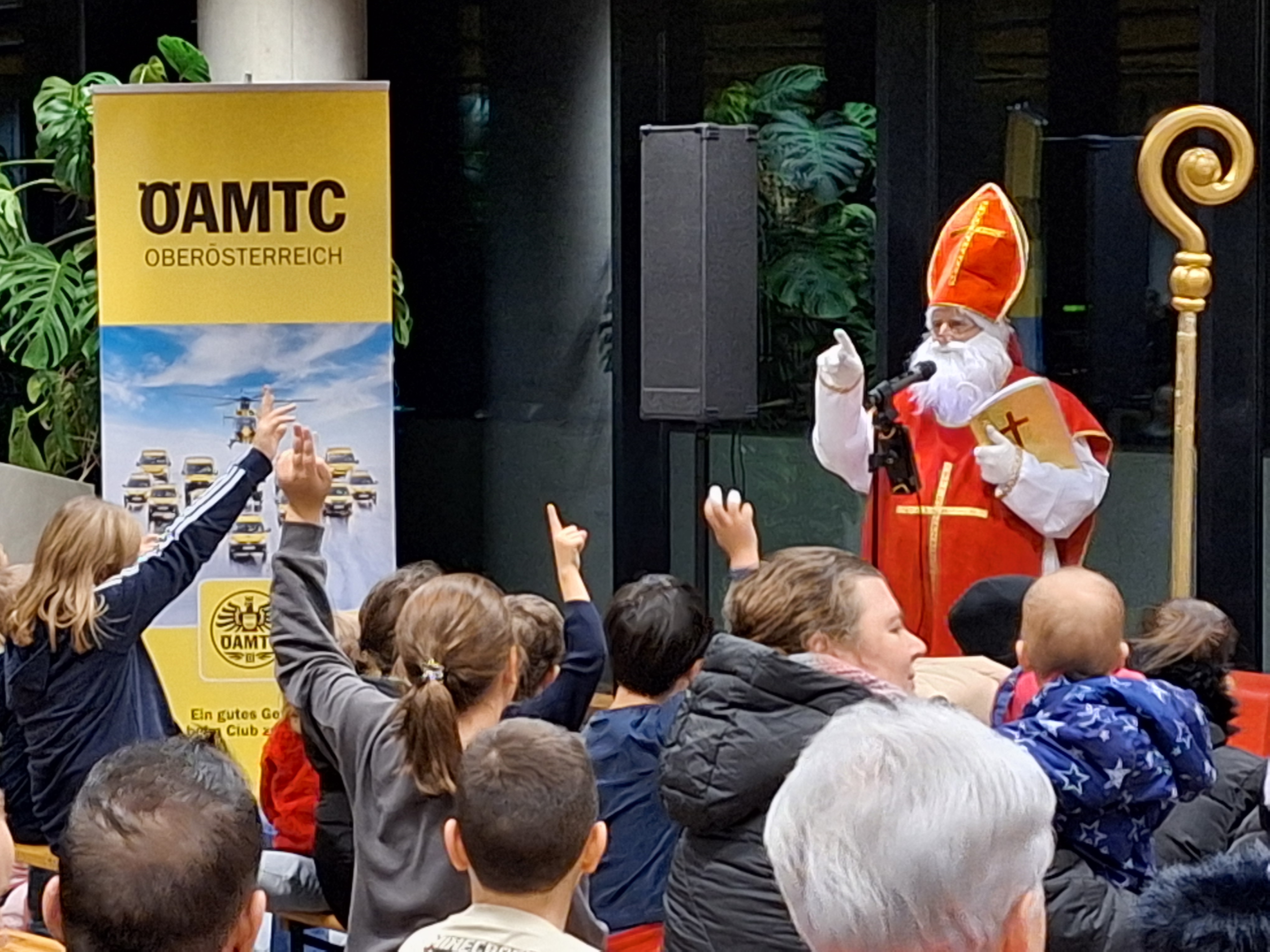 Das Foto zeigt einen Nikolaus, der vor vielen Kindern steht. Im Hintergrund ist ein ÖAMTC-Schild zu sehen.