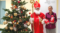 Das Foto zeigt einen Nikolaus, einen Christbaum und eine Frau, die zwei Nikolaus-Sackerl hält.