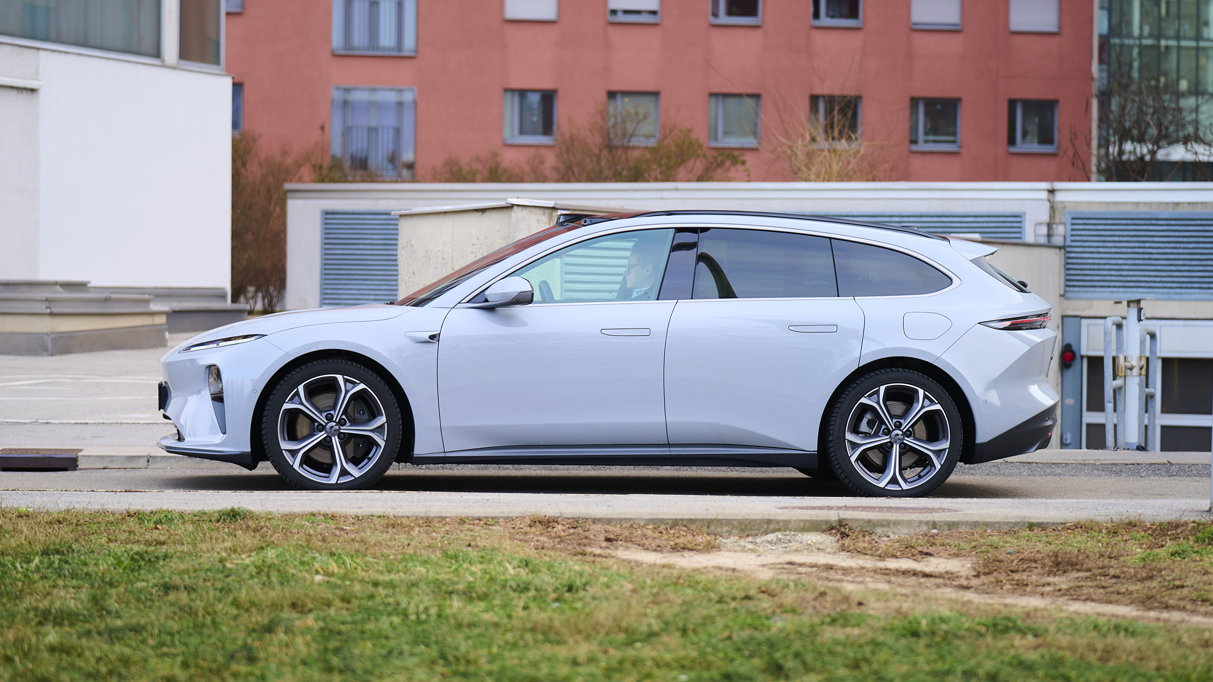 Ein hellblauer Nio ET5 Touring steht auf einer Straße durch einen urbanen Raum, im Hintergrund befindet sich ein rotes Geböude.