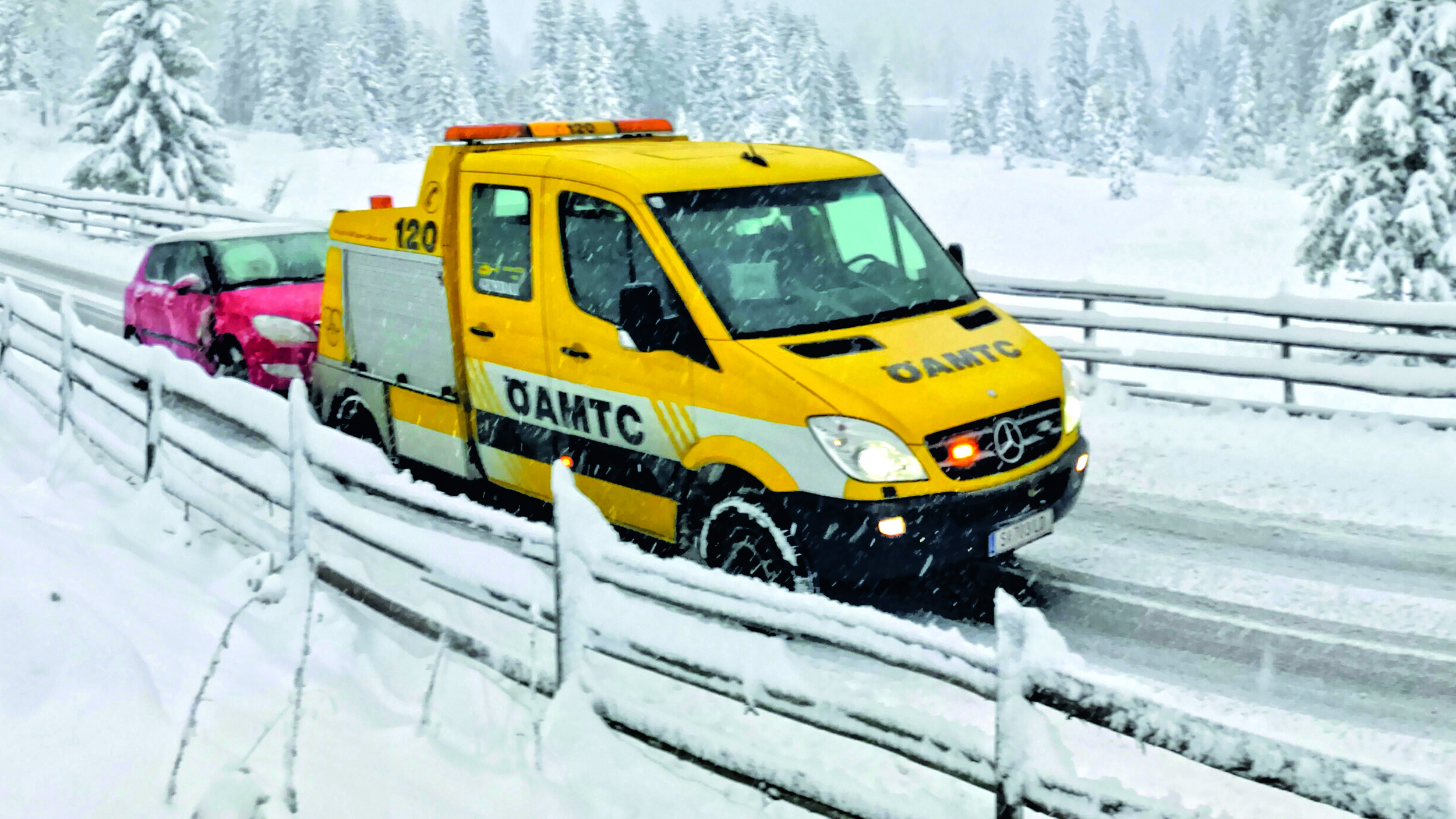 Ein ÖAMTC-Pannenfahrzeug schleppt in winterlicher Landschaft ein rotes Auto ab.