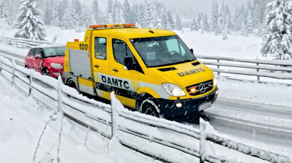 Ein ÖAMTC-Pannenfahrzeug schleppt in winterlicher Landschaft ein rotes Auto ab.
