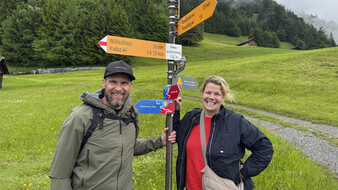 Guide und Touristin im Wander-Outfit bei einem Wander-Wegweiser.